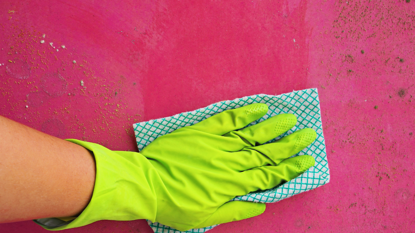 A person wearing green gloves is cleaning a pink surface with a cloth.
