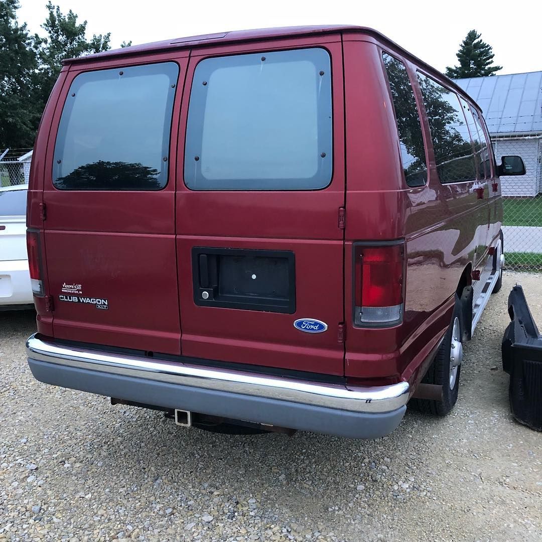 Red Ford van parked outside with two back windows and a trailer hitch.