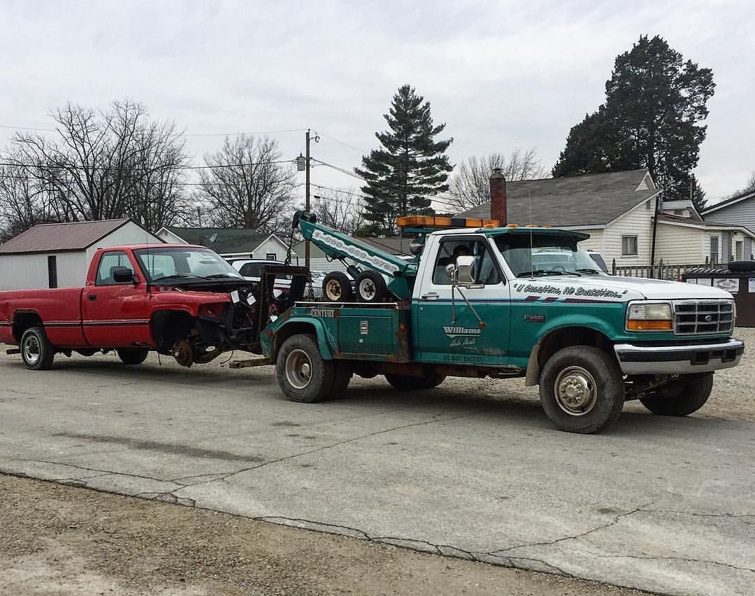 Tow truck towing a red pickup truck on a gravel road, overcast day.