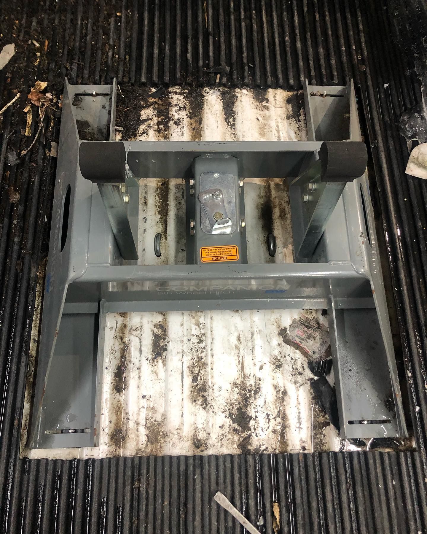 Gray metal frame with a central object and black foam blocks, inside a dirty truck bed.