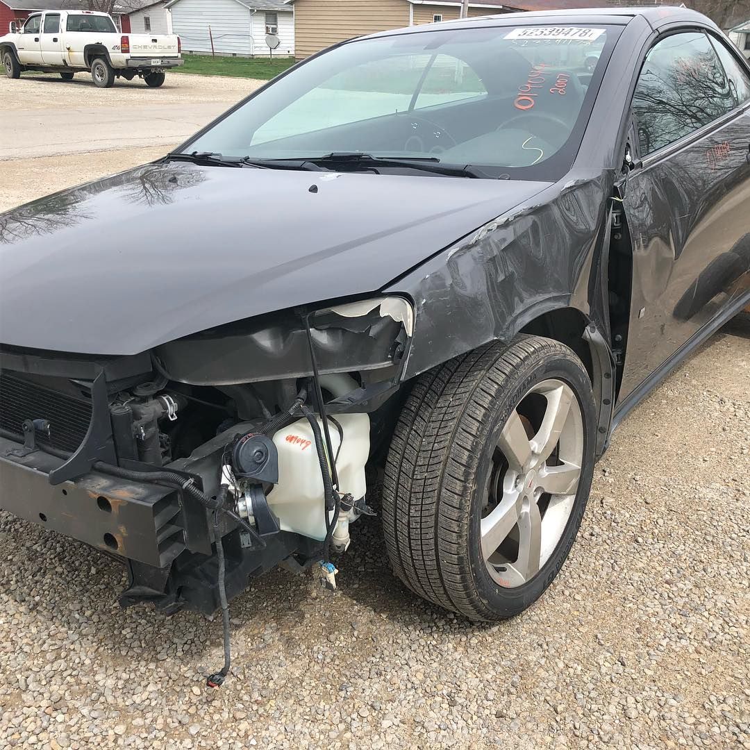 Damaged black Pontiac G6 coupe with missing front parts, parked outdoors.