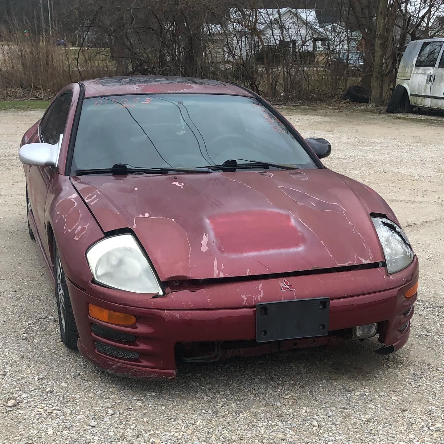 Red, weathered Mitsubishi Eclipse car with damage, parked outdoors.