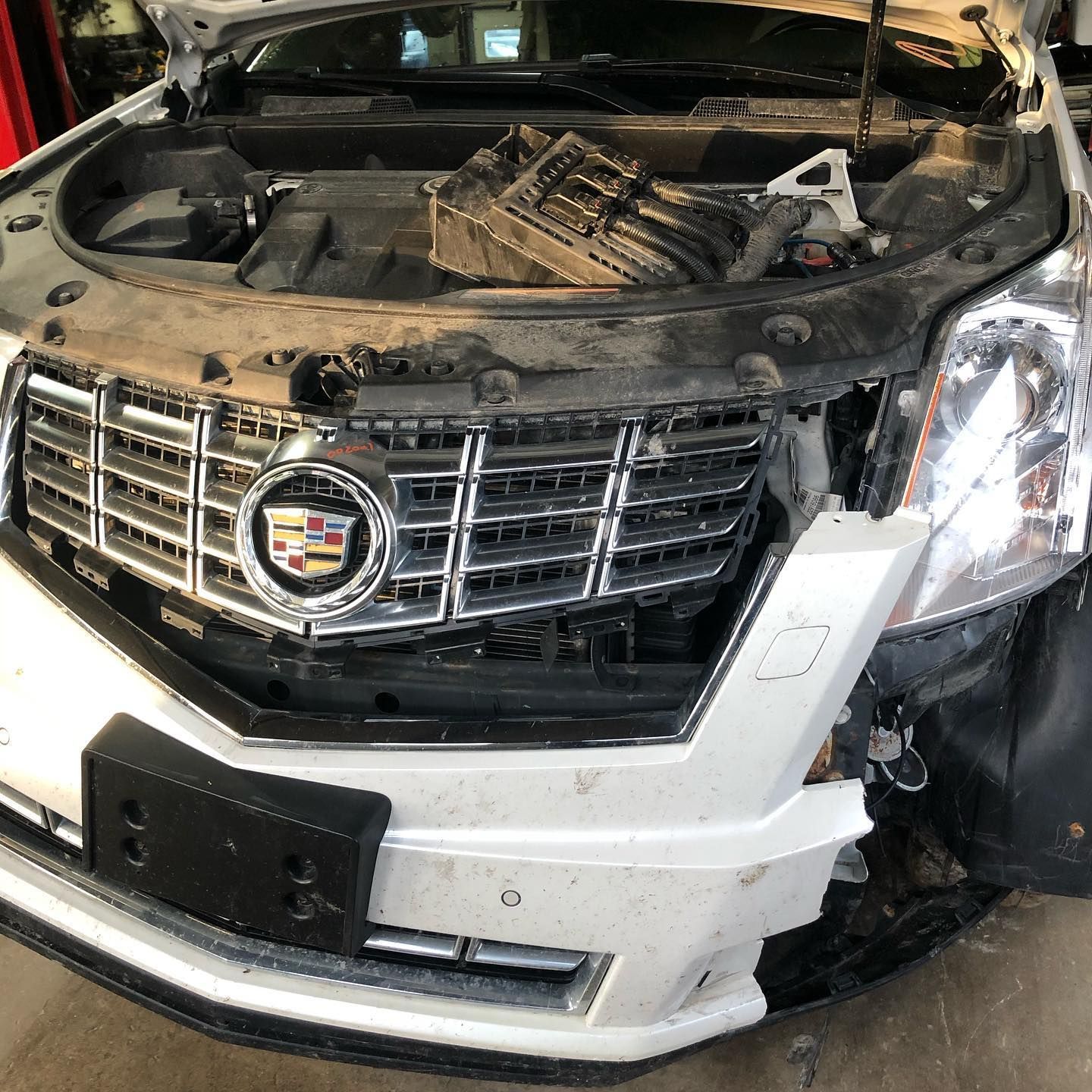 White Cadillac SRX with front-end damage; hood open, revealing engine components.