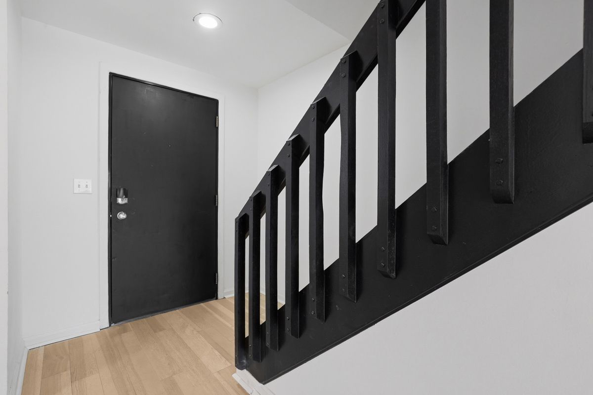Black door and staircase with black railing in a white hallway.