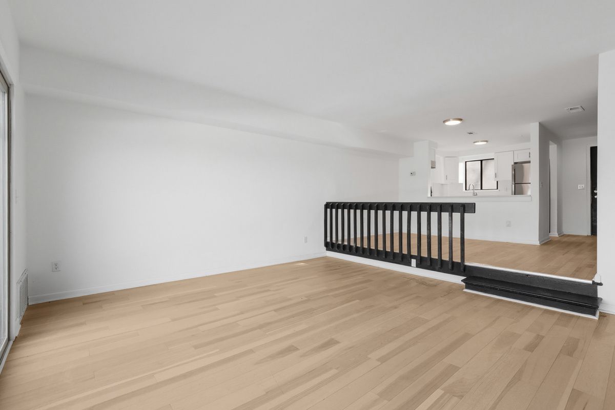 Empty room with wood floors and a partial railing leading to a kitchen area.