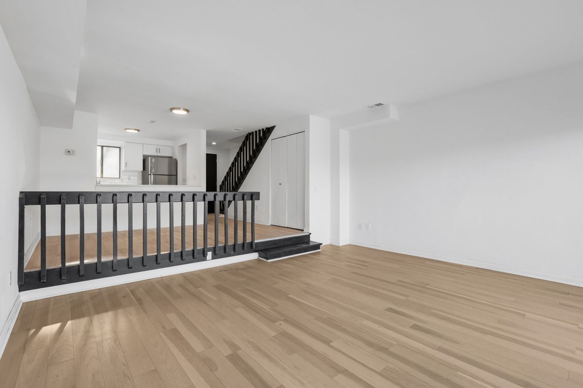 Empty interior with wooden floors, black staircase, and white walls.