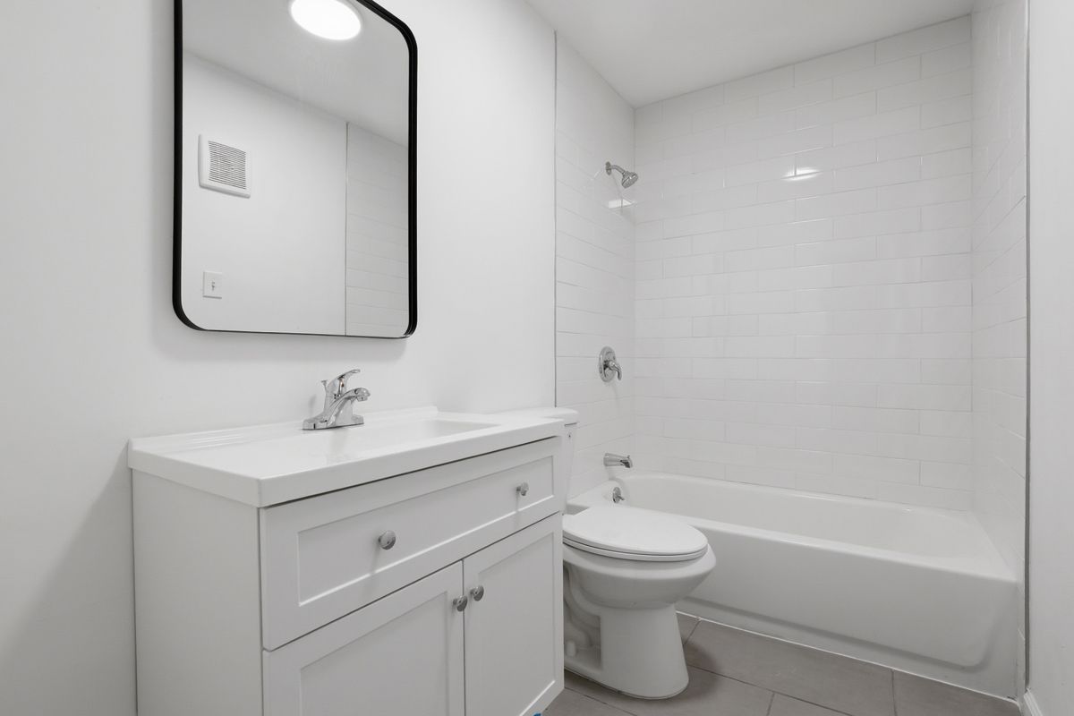 White bathroom with a vanity, toilet, and bathtub. Black framed mirror on the wall.