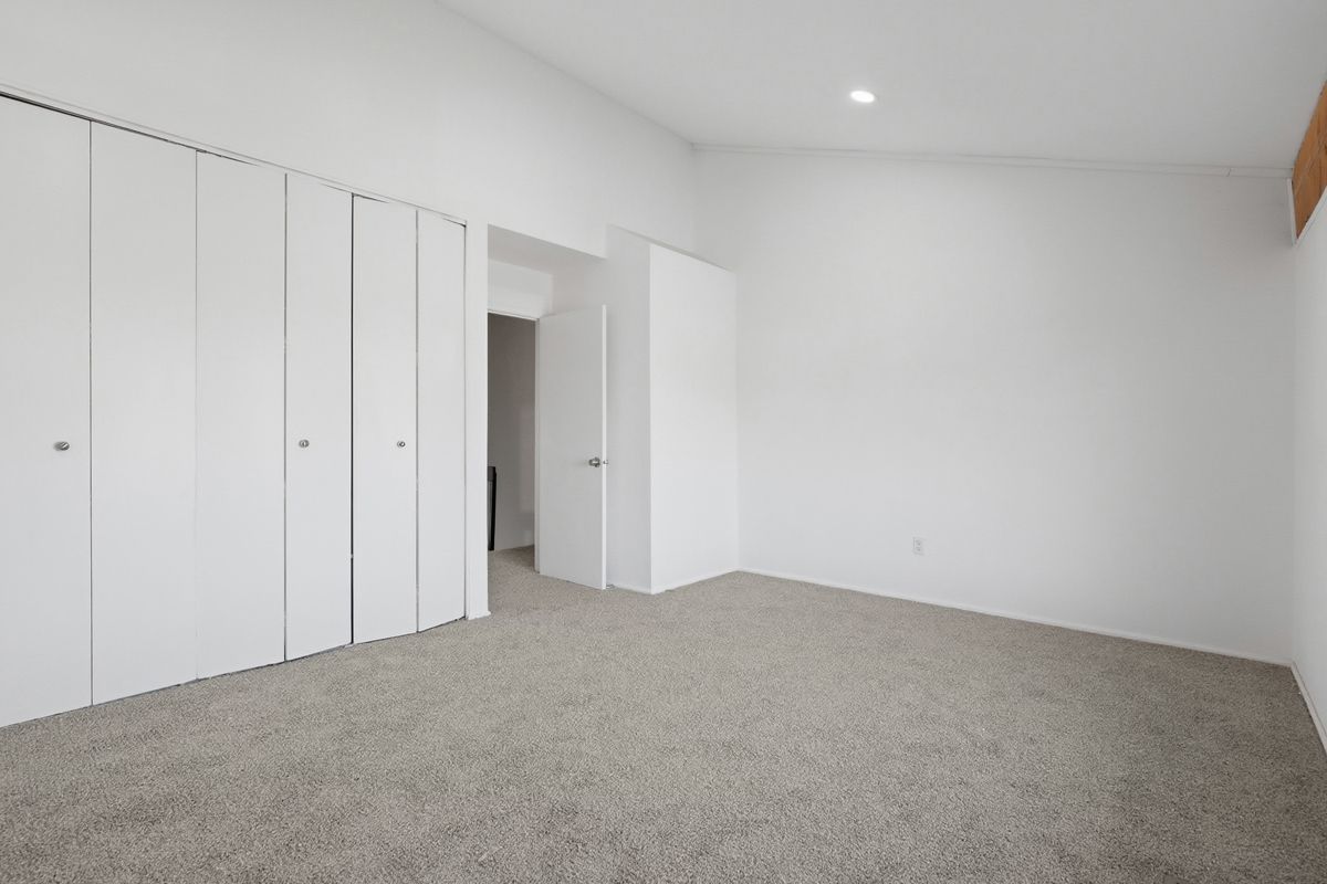 Empty, white-walled room with large closet doors and light carpet; doorway to another room.