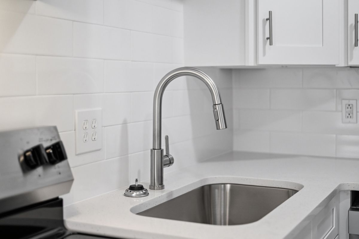 Stainless steel sink and faucet in a white kitchen with white cabinets and subway tile backsplash.
