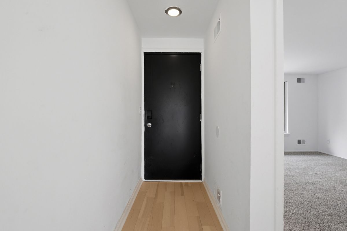 Narrow hallway with light wood floor, white walls, and a black front door.