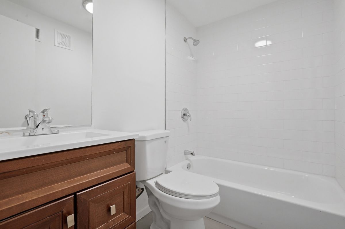 Bathroom with white tiled walls, a toilet, sink with brown vanity, and a bathtub.