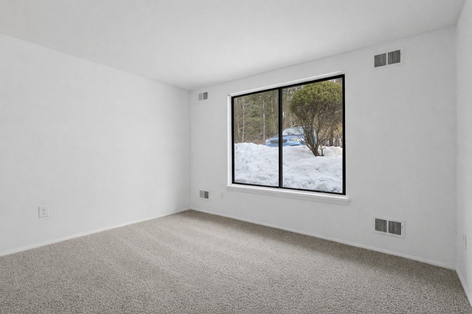 Empty room with light gray carpet, white walls, and a large window overlooking a snowy landscape.