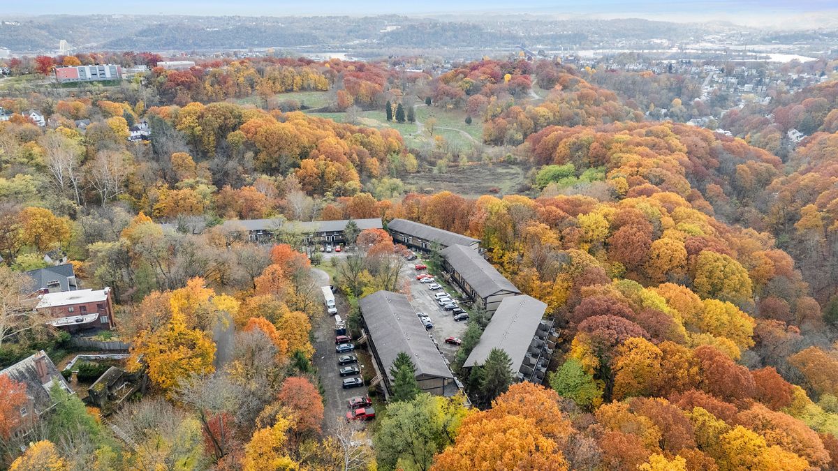 Apartment buildings nestled in a valley of trees with bright autumn foliage.