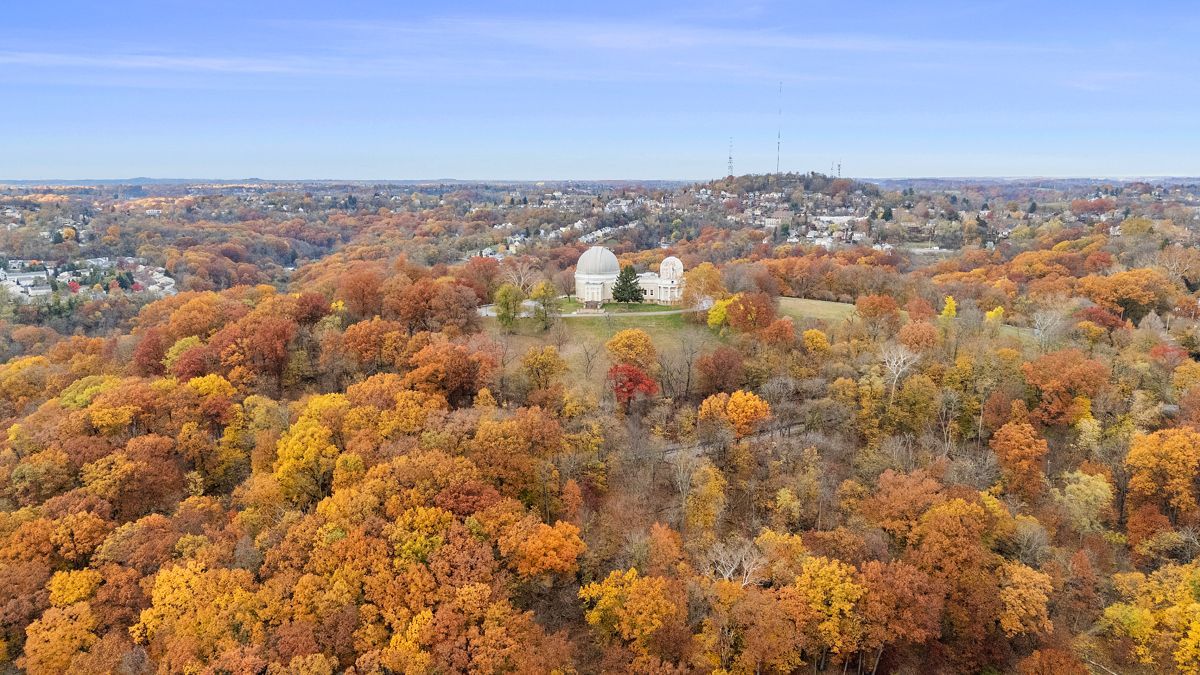 Two white domed buildings on a hillside covered in autumn foliage, under a clear blue sky.