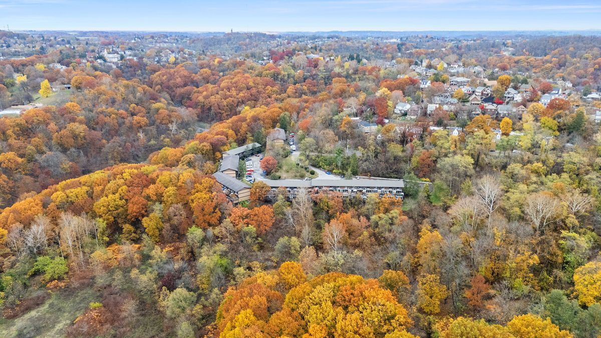 Aerial view of a building surrounded by vibrant autumn trees; houses in the background.