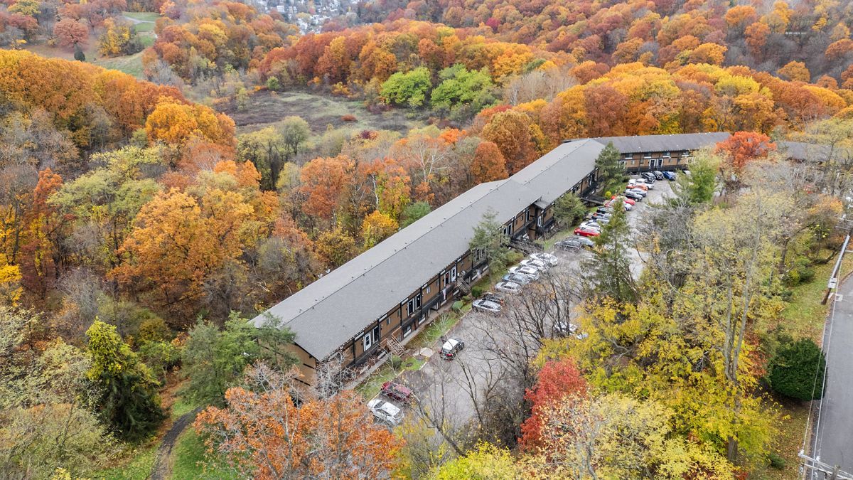Aerial view of long, low building surrounded by vibrant autumn foliage. Brown roof, trees with orange, yellow leaves.