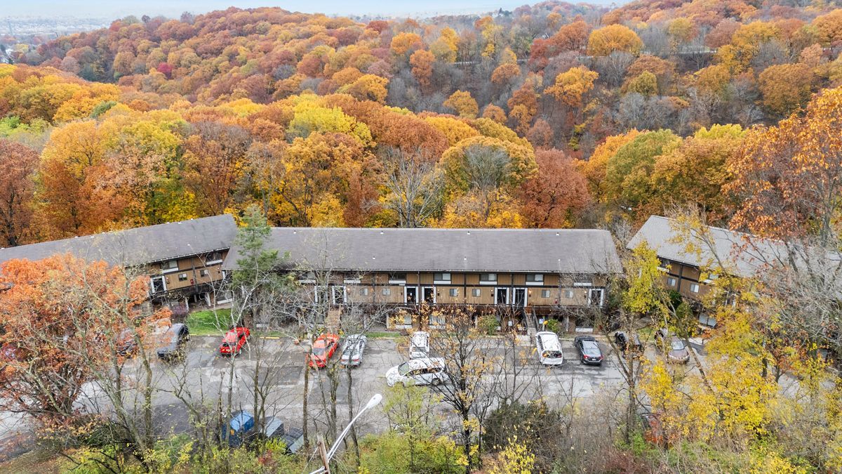 Buildings in a forest of autumn trees; parking lot with cars and trucks.
