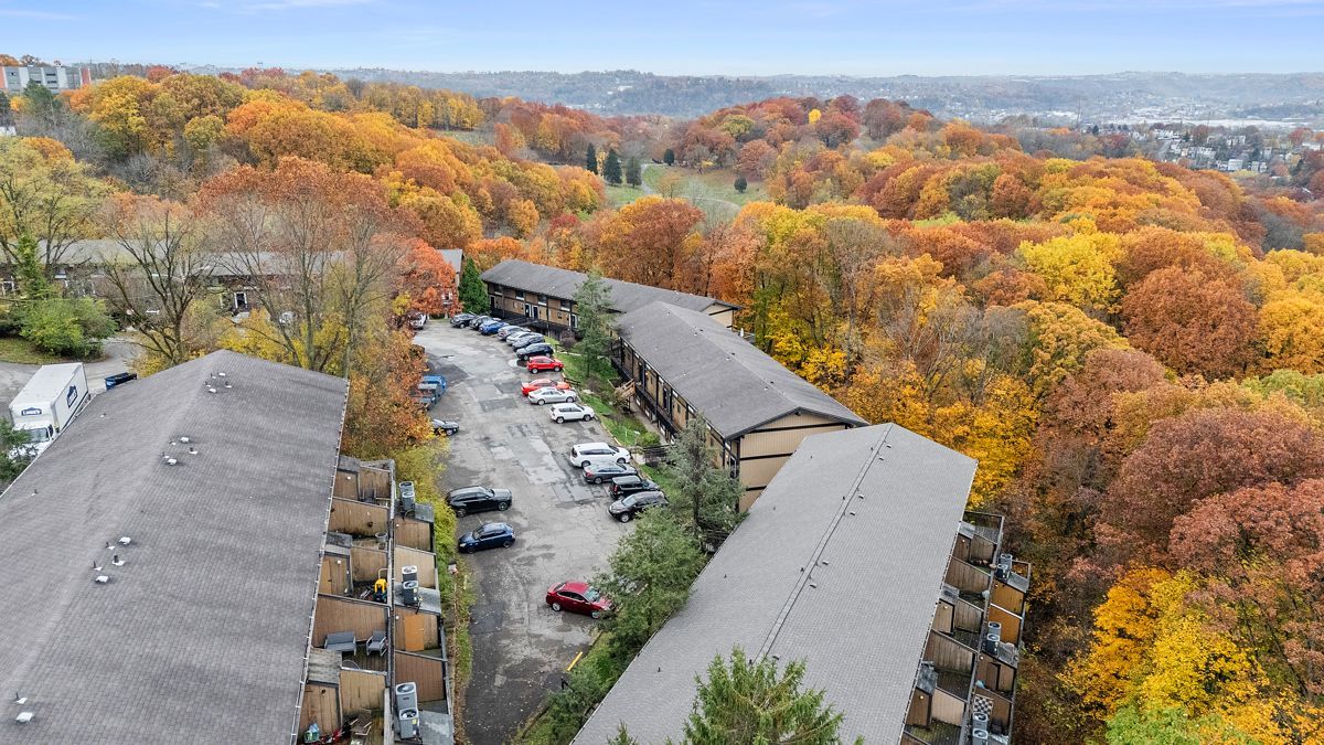 Apartment buildings with parked cars surrounded by vibrant autumn trees on a hillside.