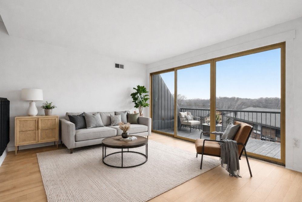 Living room with a gray sofa, rug, and large windows leading to a deck with outdoor furniture.