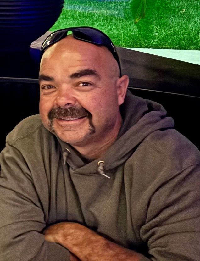 Group of men inside a bar, smiling and posing. String lights hang above a window with a city view.