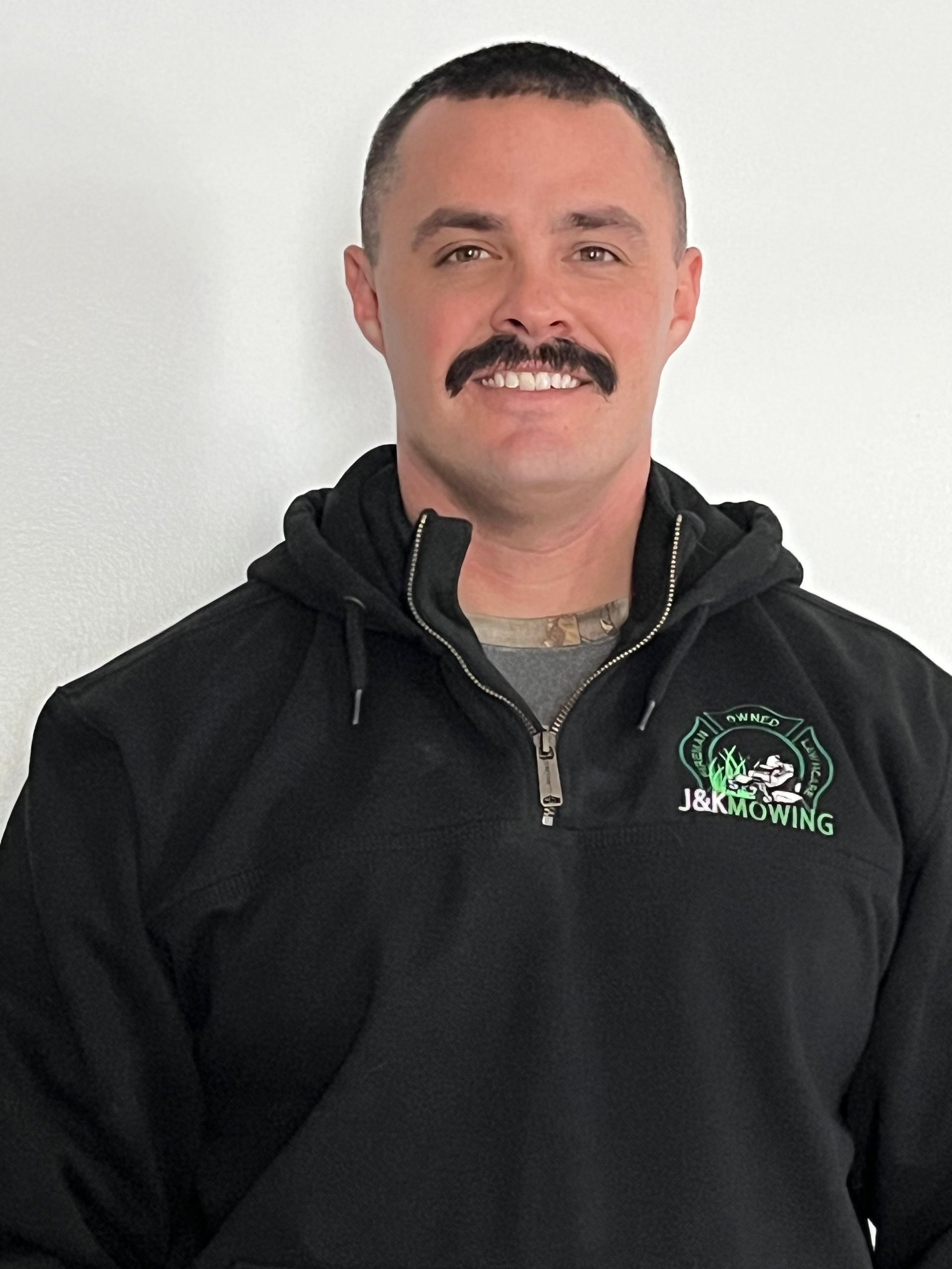 Man in black hoodie smiles, with a mustache.