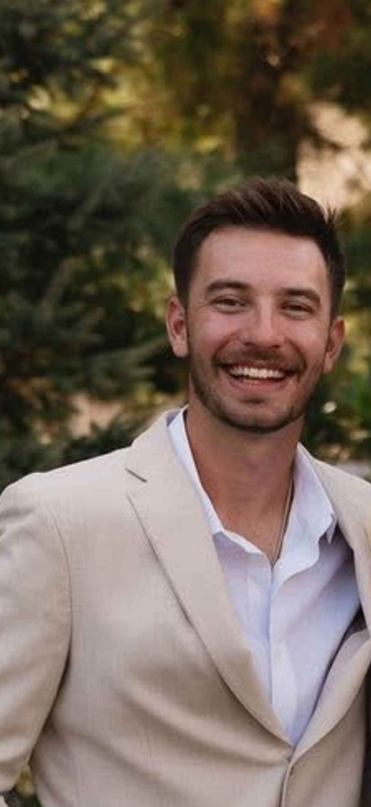 Group of men inside a bar, smiling and posing. String lights hang above a window with a city view.