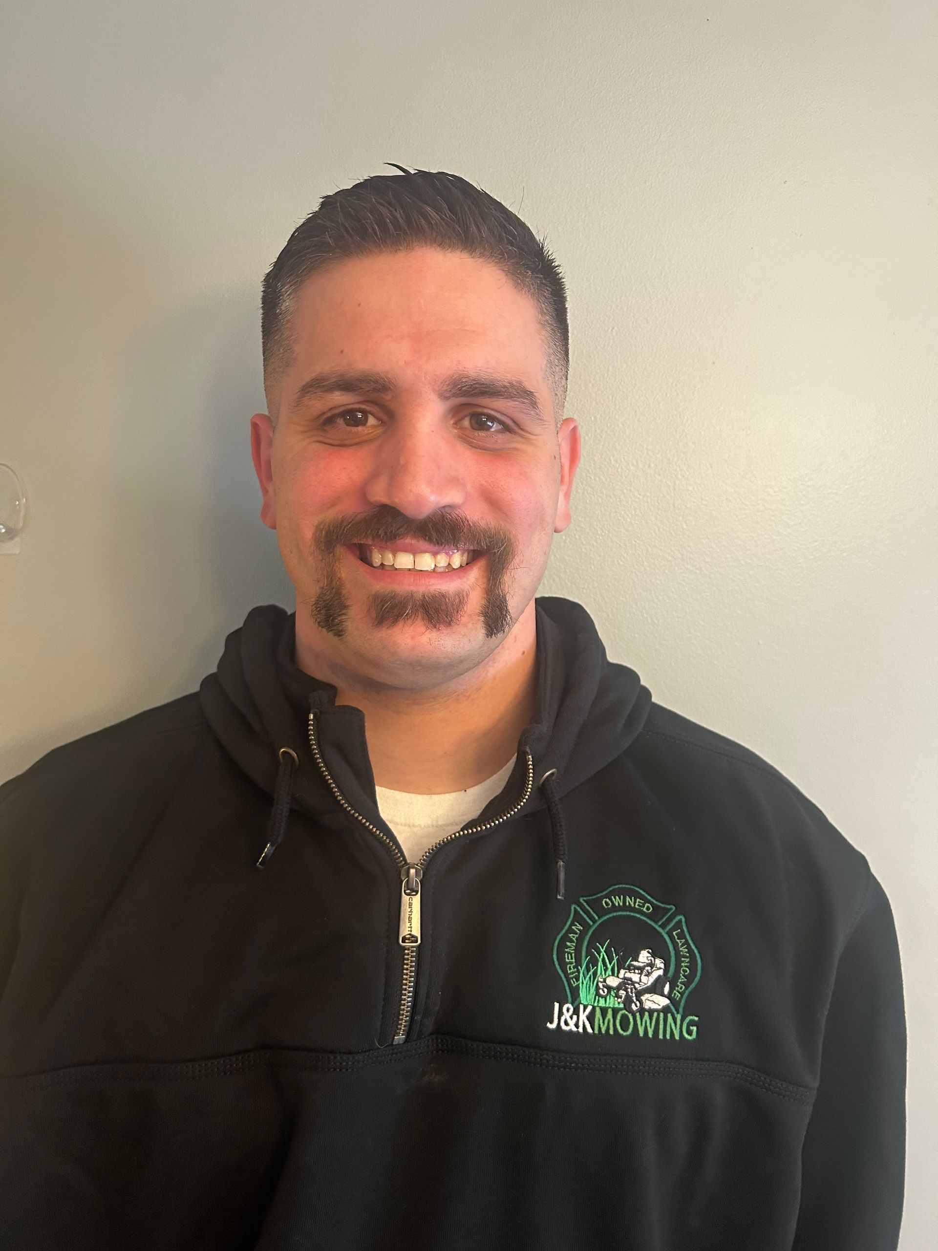 Group of men inside a bar, smiling and posing. String lights hang above a window with a city view.