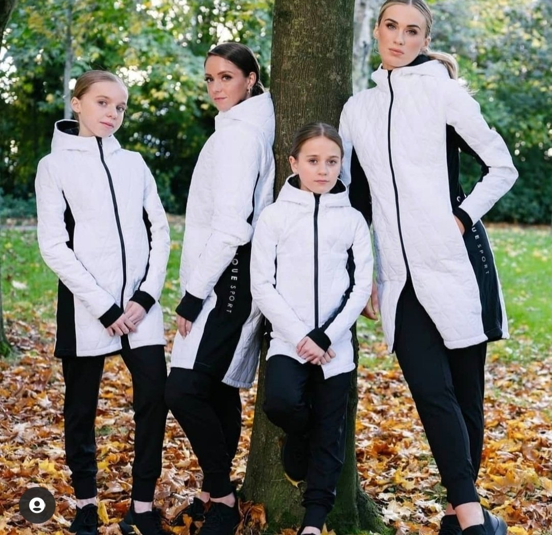 2 women and 2 girls stood against tree wearing white and black long jackets