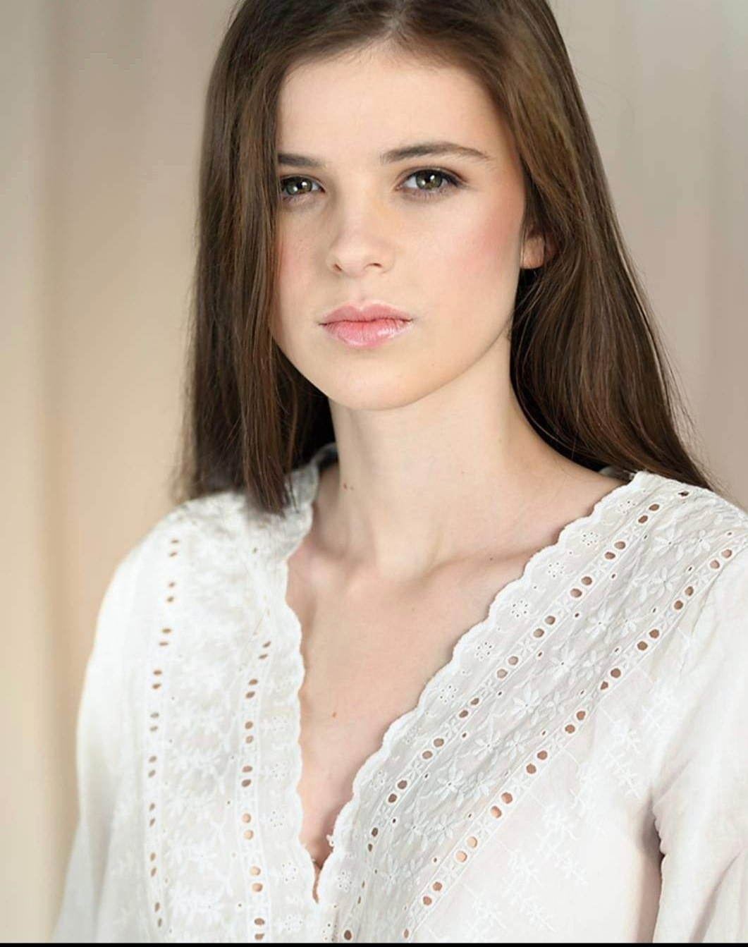 Pretty girl with brown hair and white floral top looking at camera