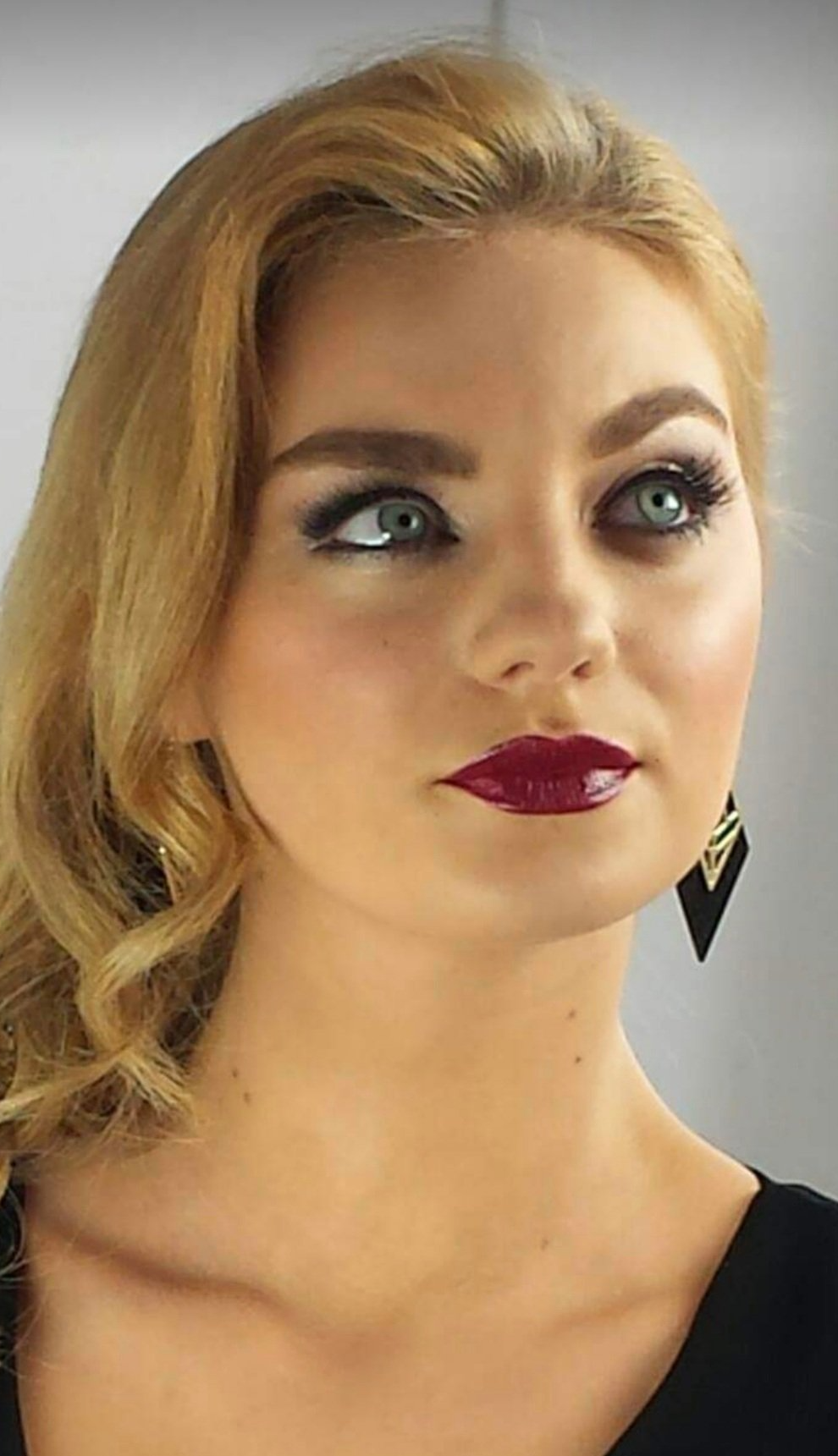 Blonde woman facing camera and looking upwards to show big lashes and red lips