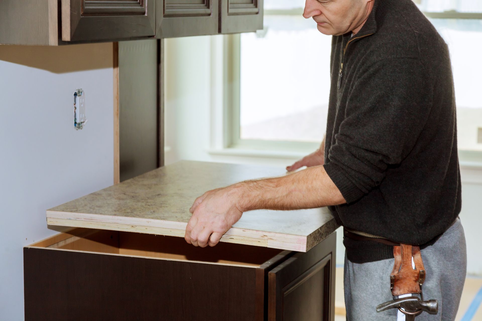 A man carefully installs a countertop in a kitchen, using tools and measuring for precision.