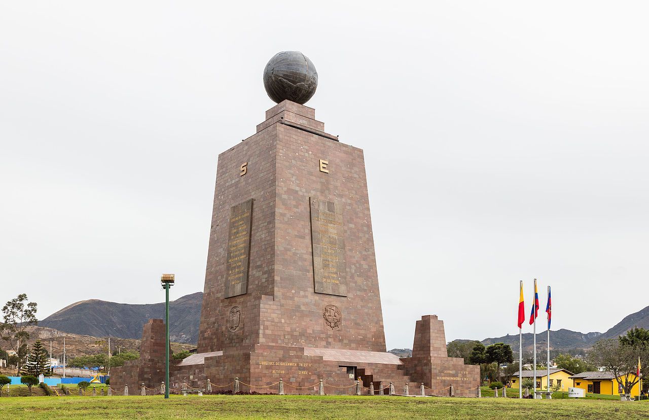 A large stone statue with a globe on top of it. Ciudad Mitad del Mundo