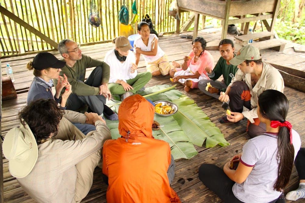 A group of people are sitting in a circle on the floor eating food.