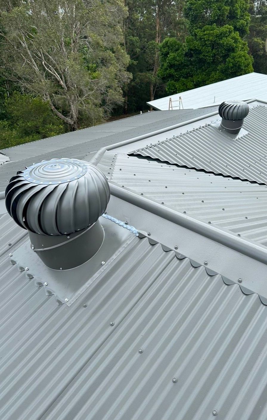 A Gray Corrugated Metal Roof With Two Spinning Whirly Bird — Whirly Bird King in Strathpine, QLD