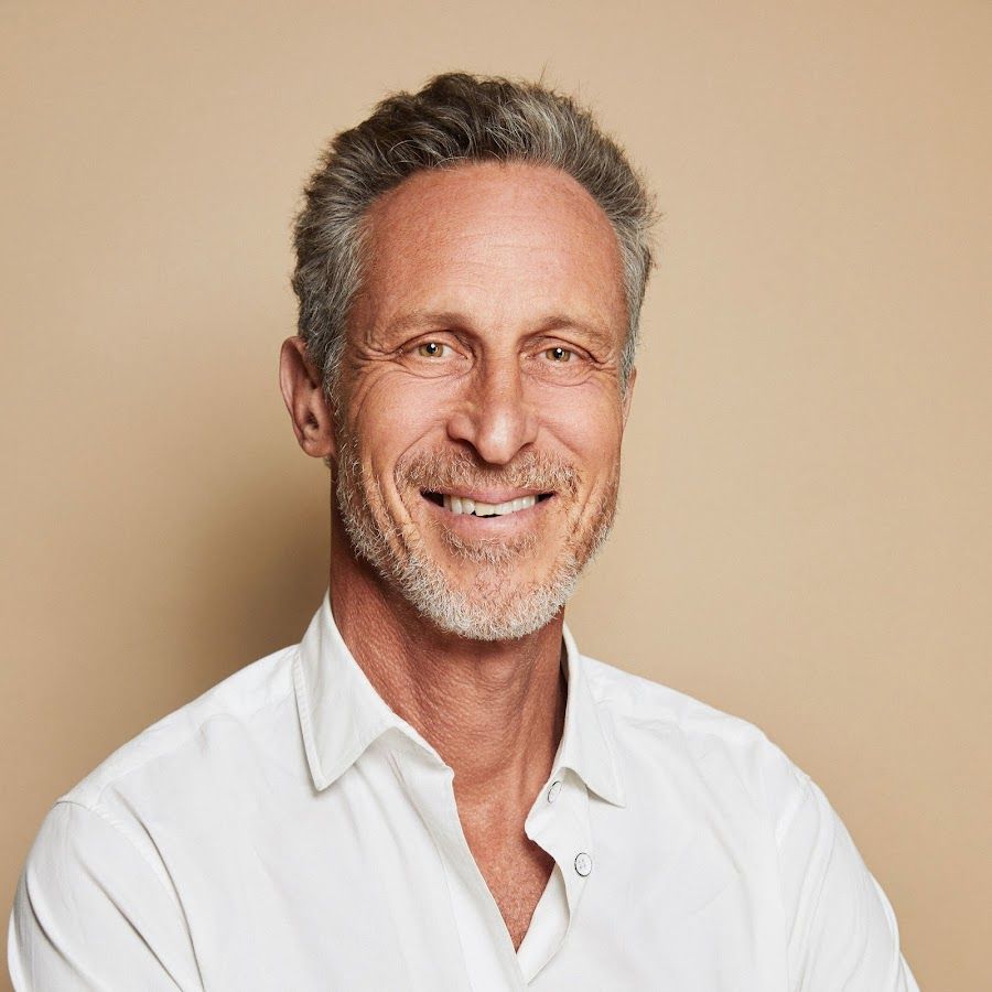 A man with a beard is wearing a white shirt and smiling.