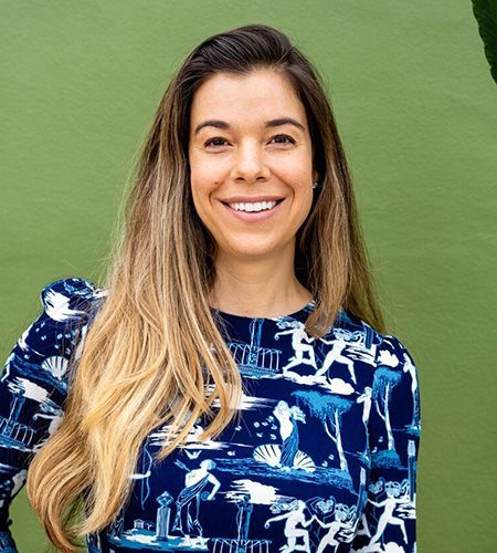 A woman is smiling for the camera while wearing a blue and white floral shirt.