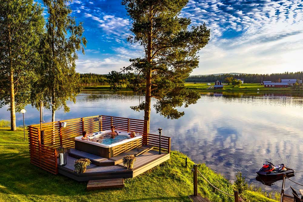 A hot tub is sitting on a deck next to a lake.
