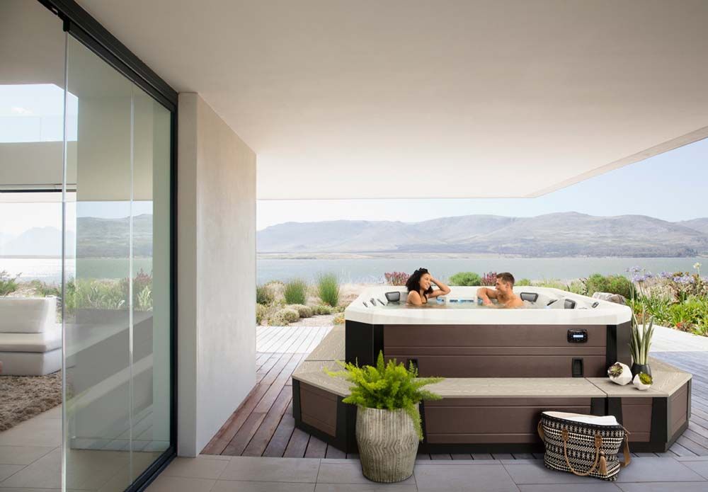A couple is sitting in a hot tub on a balcony overlooking a lake.