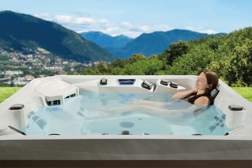 A woman is laying in a hot tub with mountains in the background.