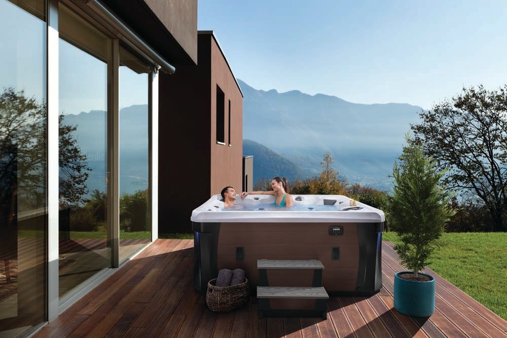 A couple laying in a hot tub on a deck with mountains in the background