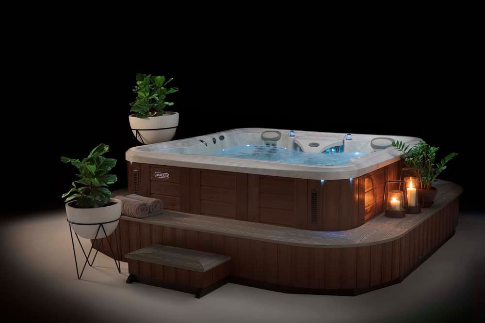 A hot tub is sitting on top of a wooden platform next to potted plants and candles.