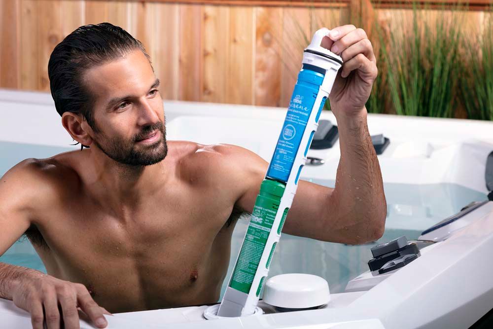 A shirtless man is sitting in a hot tub holding a bottle of shampoo.