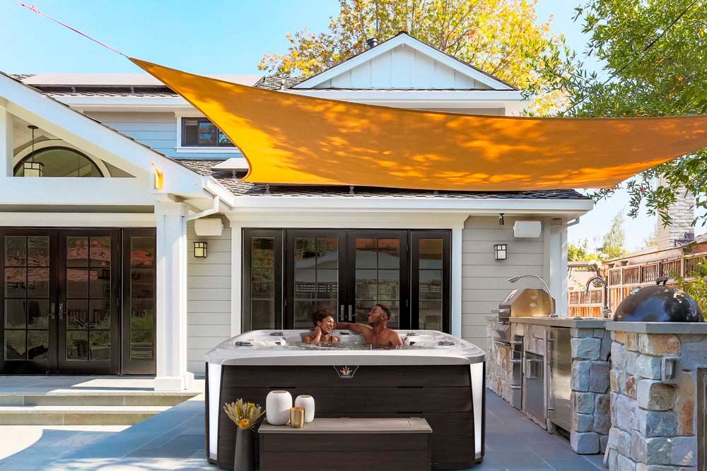 A couple is sitting in a hot tub under a shade sail.