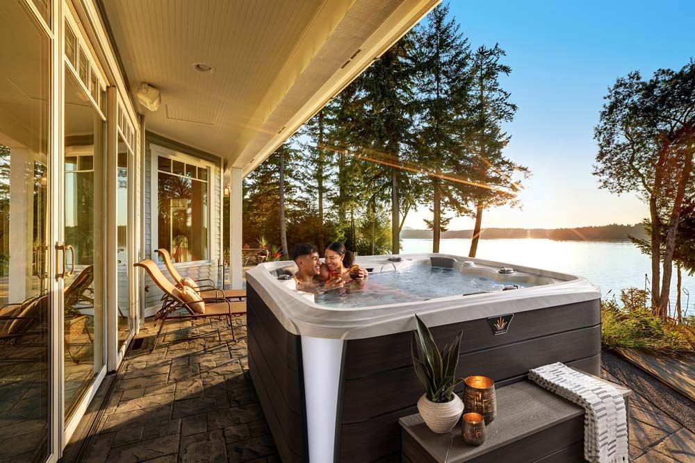A couple is sitting in a hot tub on a patio overlooking a lake.