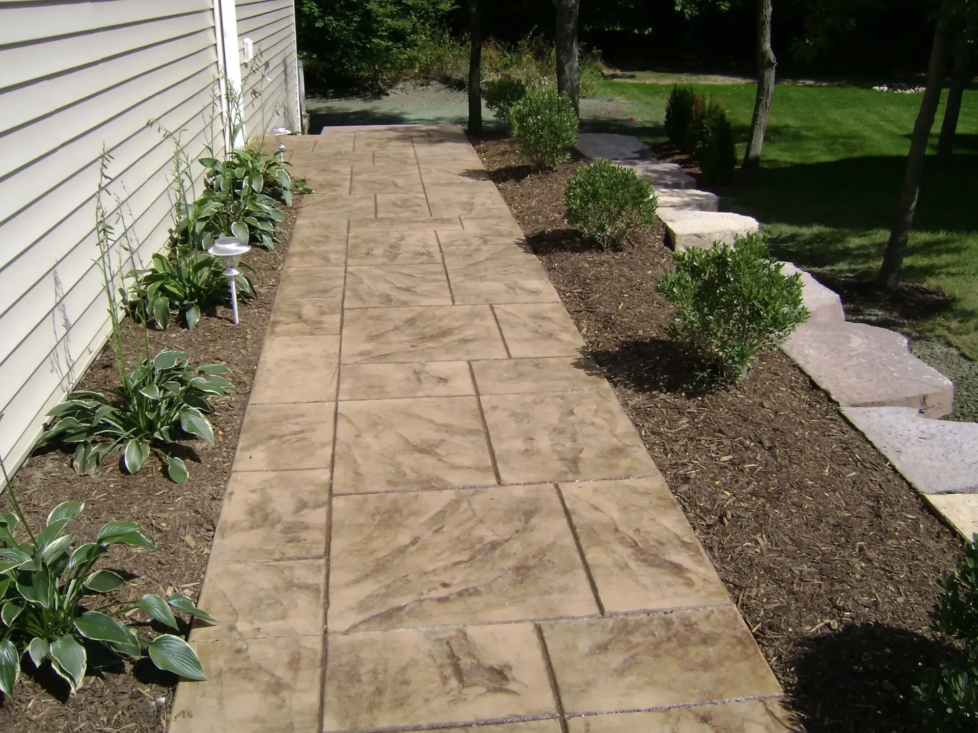 Stamped concrete walkway through a landscaped yard, alongside a building.
