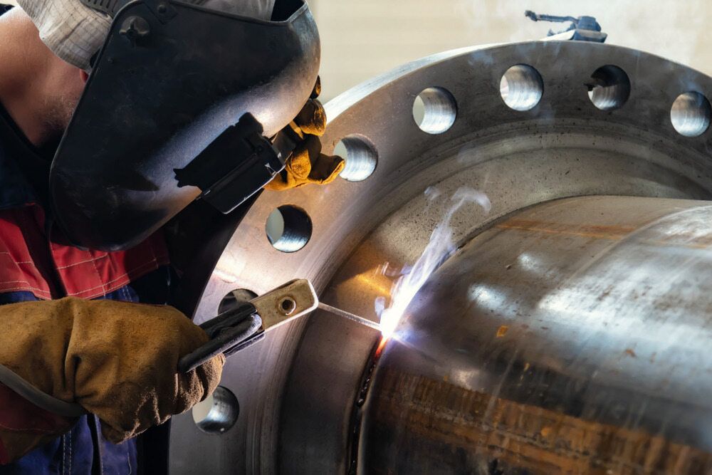 A Man Wearing a Welding Mask is Welding a Metal Pipe — LM Engineering In Mareeba, QLD