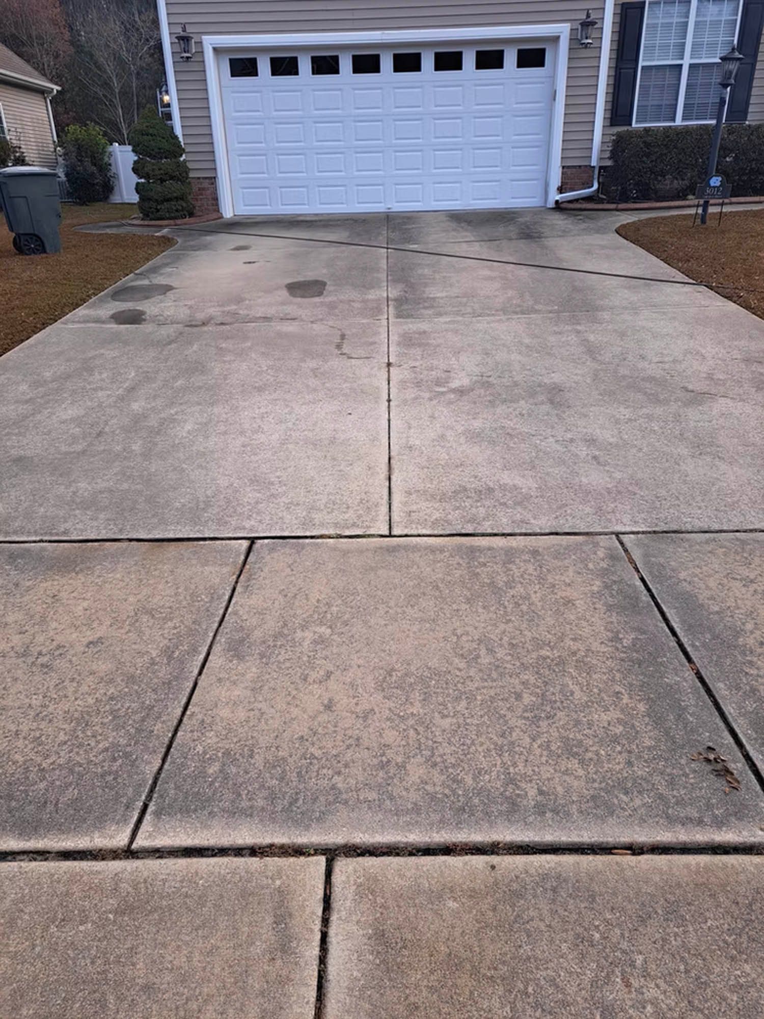A concrete driveway in front of a house with a white garage door.