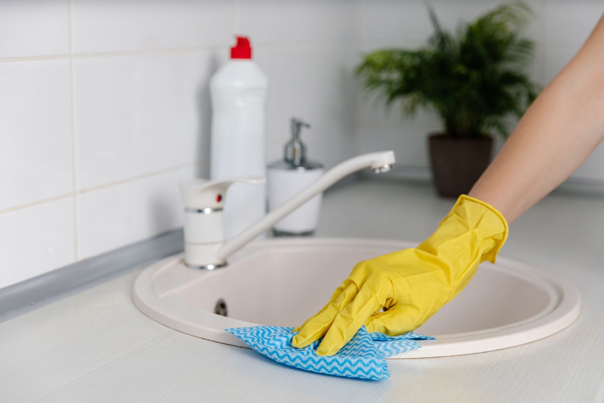 A Person Wearing Yellow Gloves is Cleaning a Kitchen Sink With a Cloth