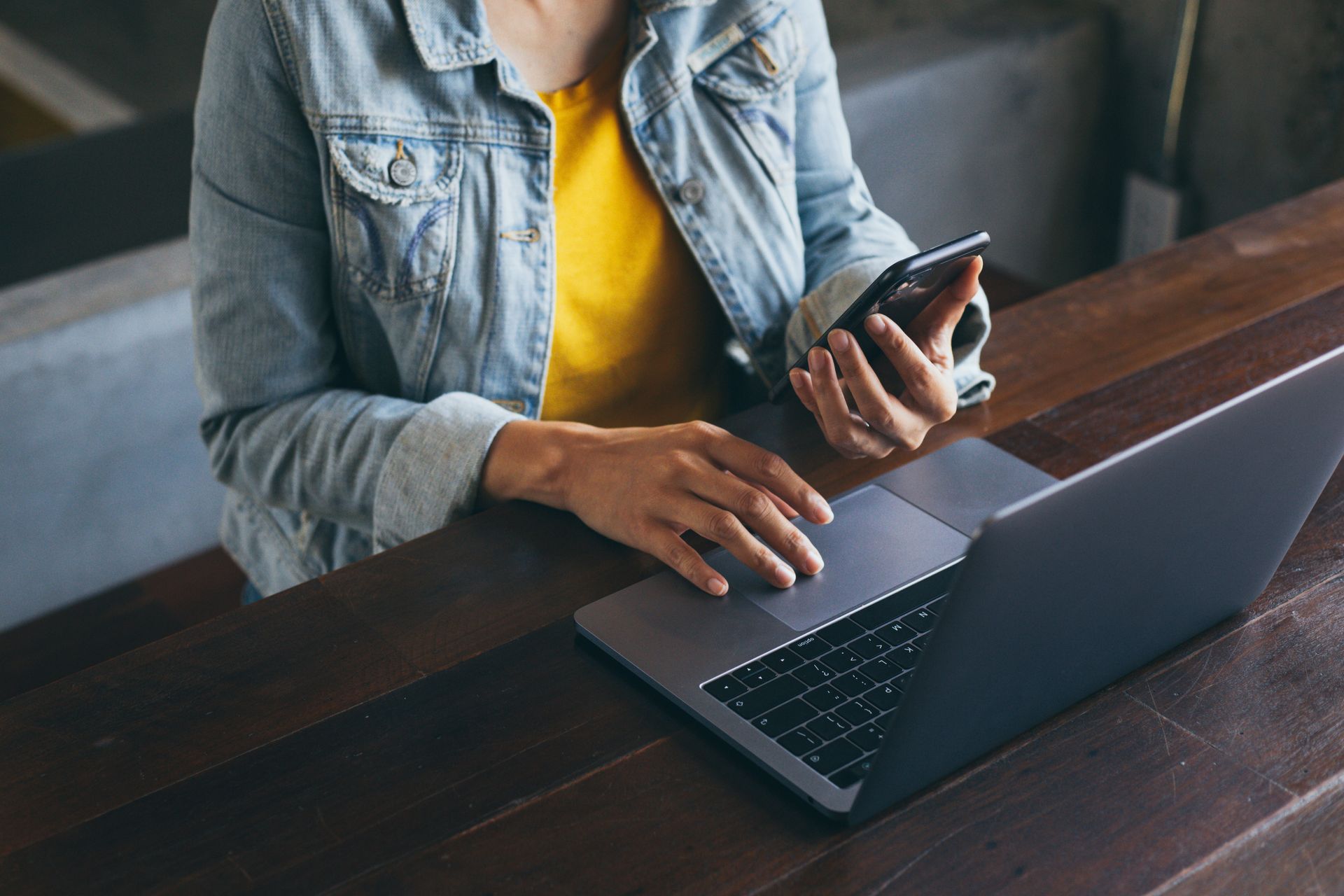 Une femme est assise à une table en utilisant un ordinateur portable et un téléphone portable.