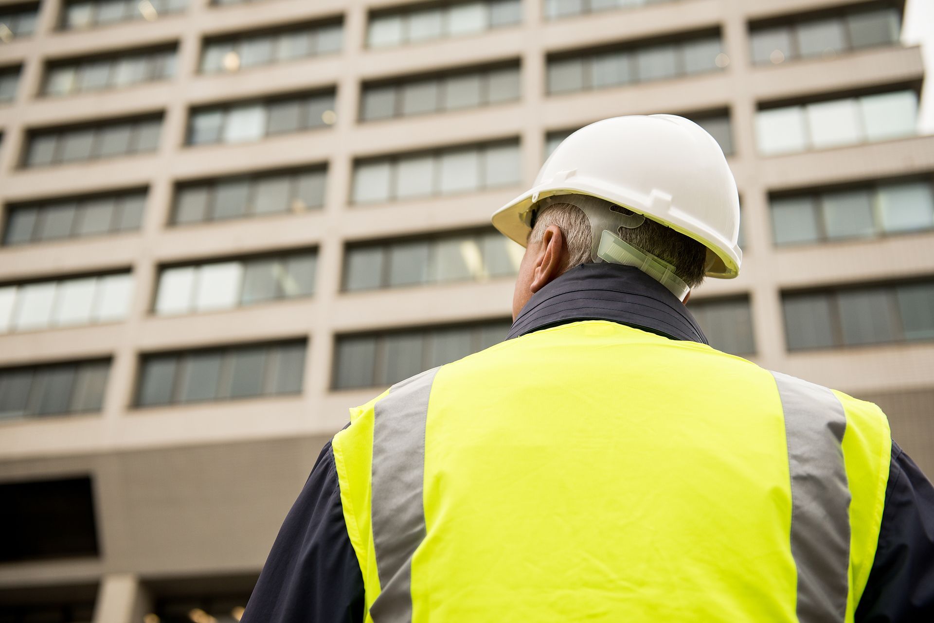 A man wearing a hard hat and a yellow vest is standing in front of a building.